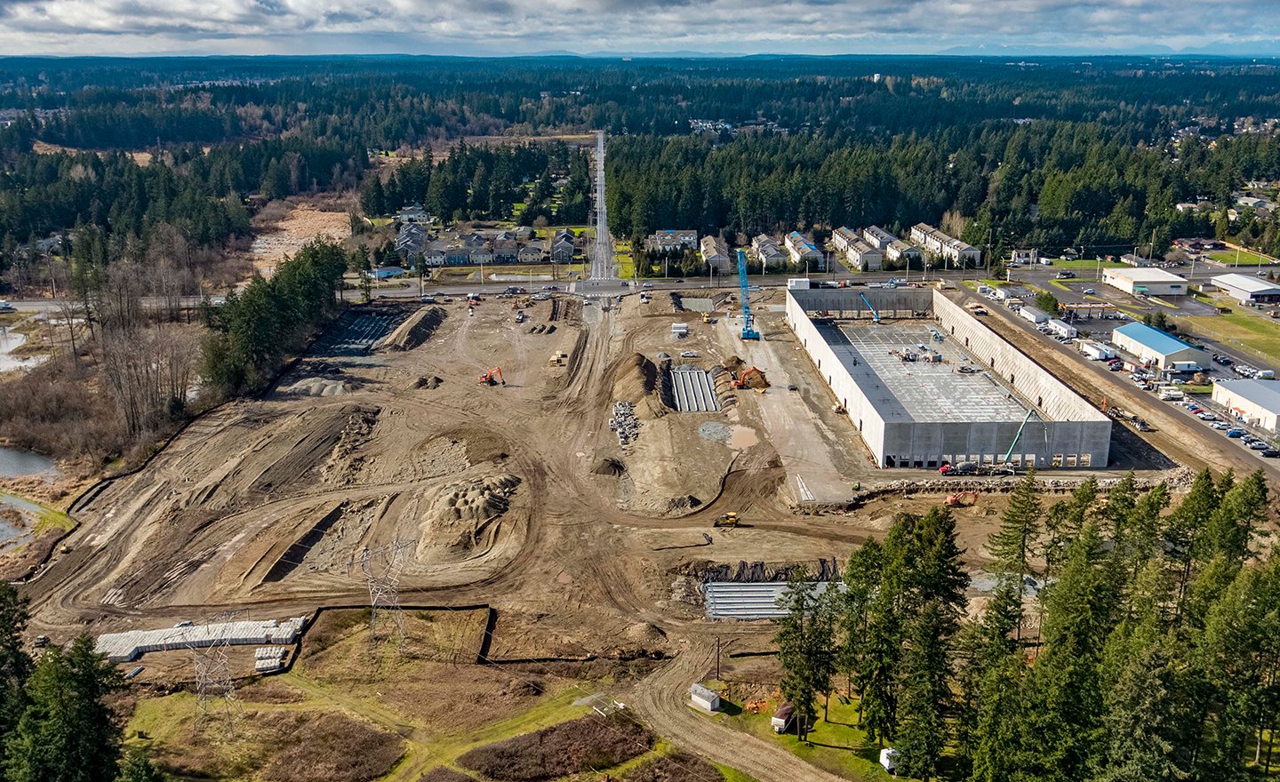 Bir şantiyede lojistik faaliyetleri; vinçle malzeme taşıma, iş makineleri ve çalışanlar koordineli şekilde çalışıyor.