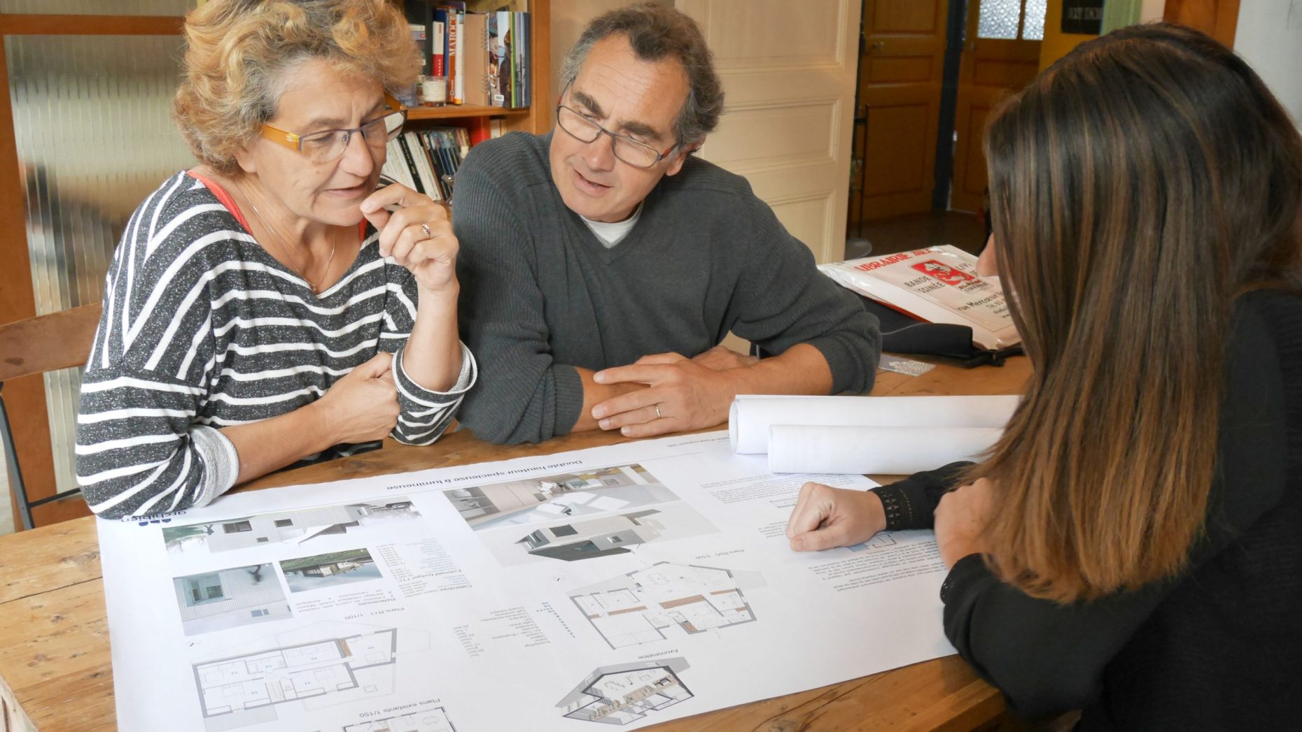 Ankara’daki mimarlık ofisleri arasında seçim yapan bir ekip; masa üzerinde proje paftaları, plan çizimleri, malzeme örnekleri ve bilgisayar yer alıyor.