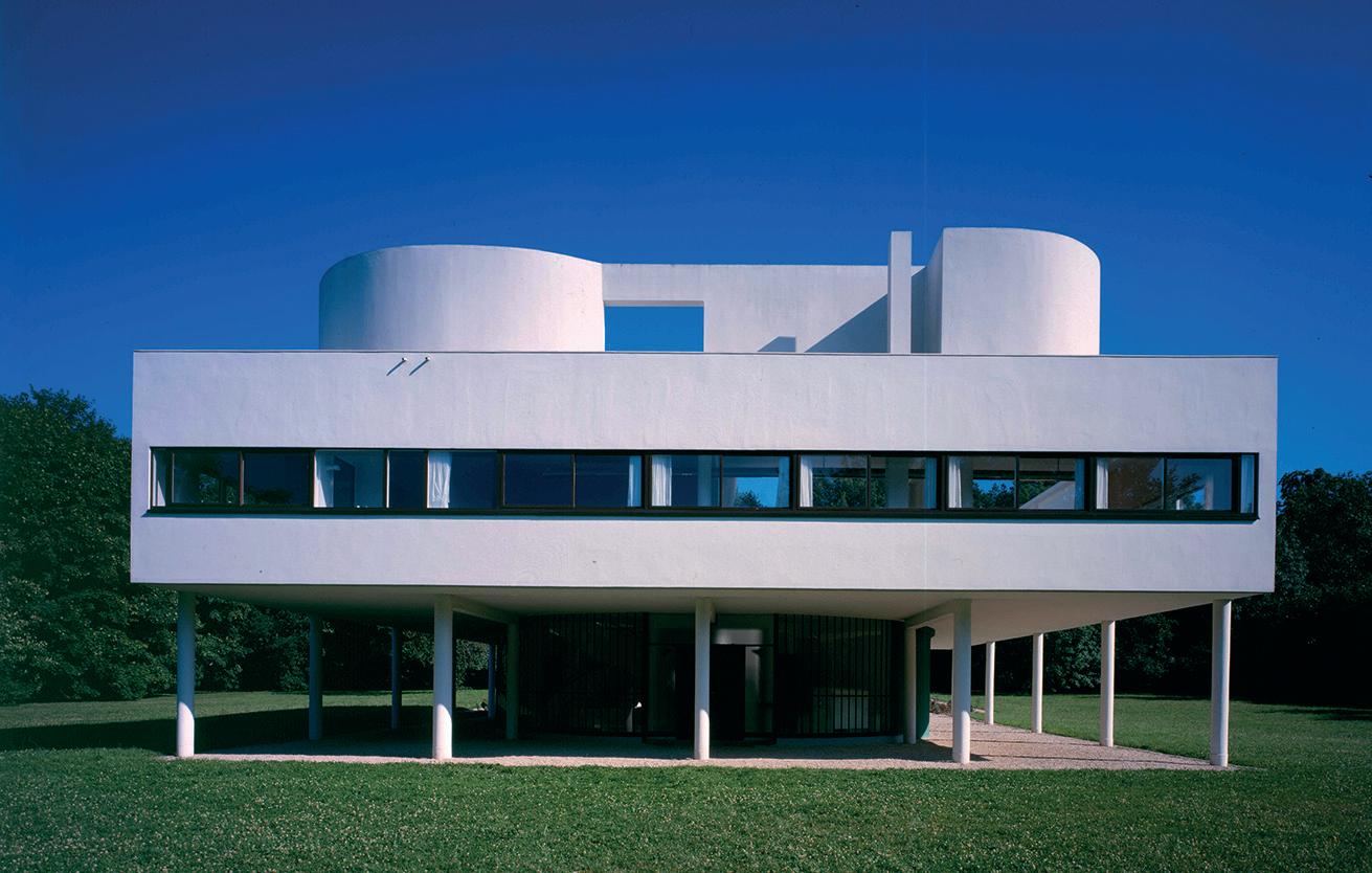 Villa projesinin tasarım sürecini değerlendiren mimarlık ekibi; masa üzerinde plan çizimleri, cephe eskizleri, malzeme örnekleri ve bilgisayar yer alıyor.